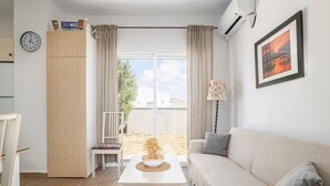 Una sala de estar con un sofá, una mesa de centro, un armario de madera, una silla, un reloj y una ventana con cortinas.