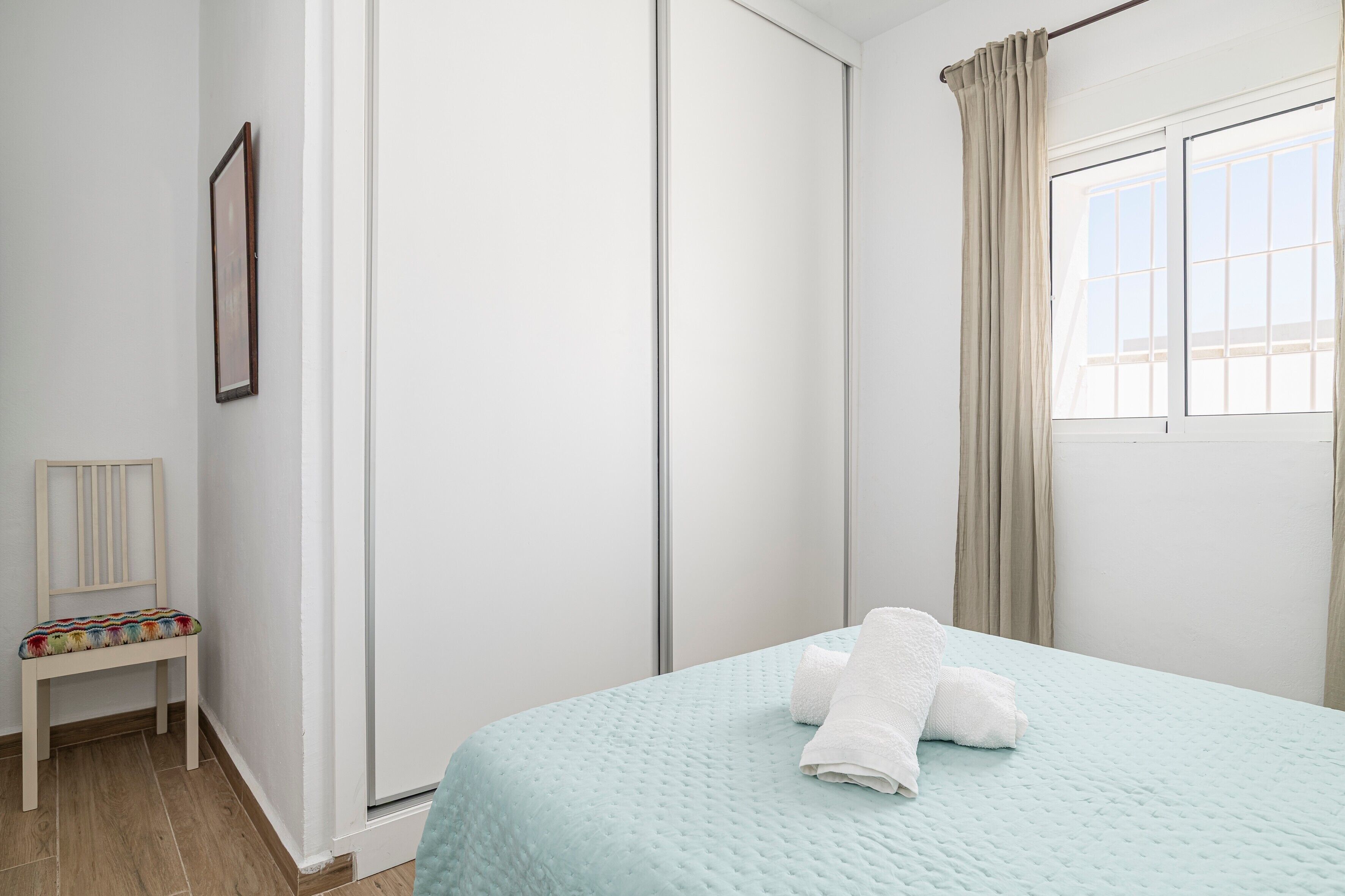Een slaapkamer met een bed, een stoel, een kledingkast en een raam met gordijnen.
