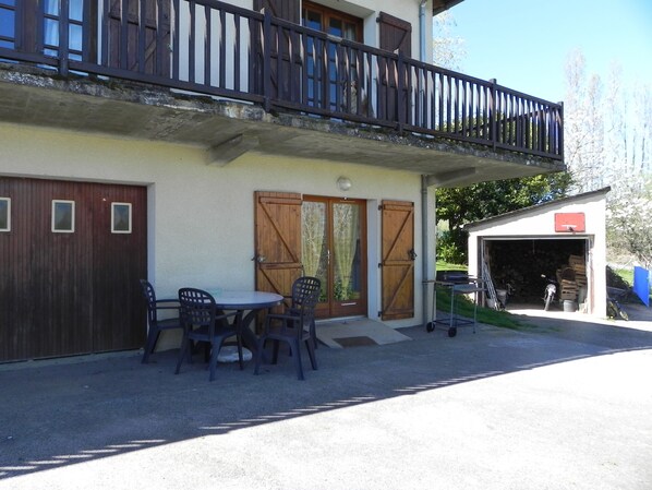 Un bâtiment à deux étages doté d’un balcon, d’un garage et d’une table avec des chaises à l’extérieur.