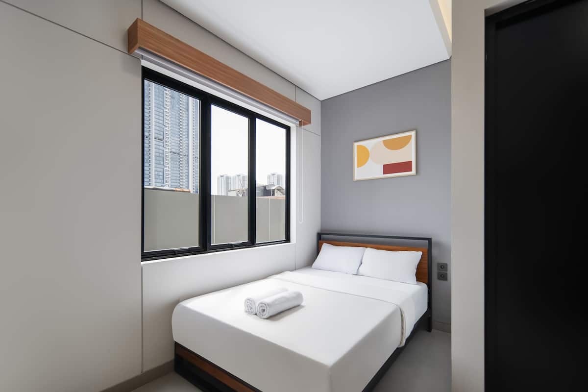 A modern hotel room with a large window, a bed with white linens, and a city view.