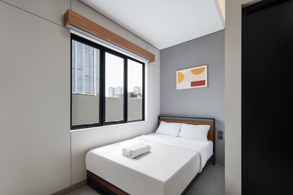 Een moderne hotelkamer met een groot raam, een bed met witte lakens en uitzicht op de stad.