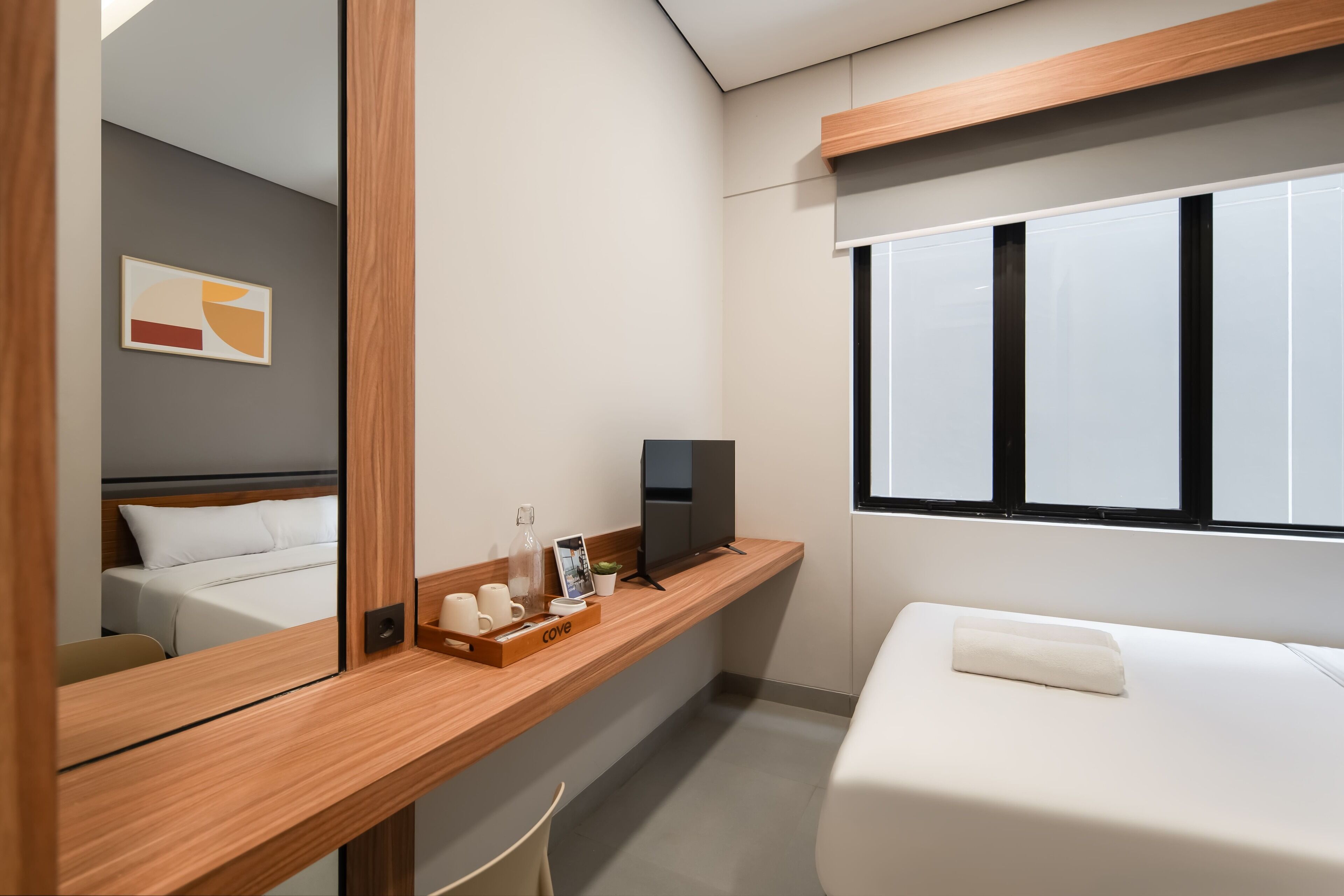 Camera d'albergo moderna con una scrivania in legno, una televisione a schermo piatto, un letto e un'ampia finestra.
