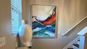 Een hal met een moderne trap, een groot abstract schilderij aan de muur en een witte vaas op een glazen tafel.