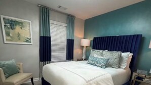 Een slaapkamer met een groot bed, een nachtkastje, een lamp, een stoel en een plafondventilator.