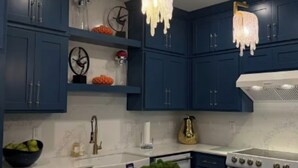Een moderne keuken met donkerblauwe kastjes, witte aanrechtbladen en een centraal eiland met een schaal groene groenten.