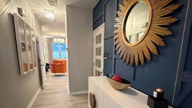 Een hal met een witte console tafel, een grote zonspiegel en een deur naar een kamer met een blauwe accentmuur.
