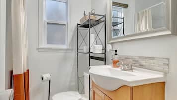 Une salle de bain avec un lavabo blanc, un meuble-lavabo en bois, un miroir, des toilettes et une fenêtre avec un rideau.