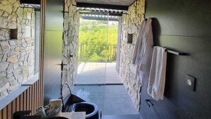 Ein modernes Badezimmer mit Steinwänden, Holzboden und Blick auf Grünflächen.