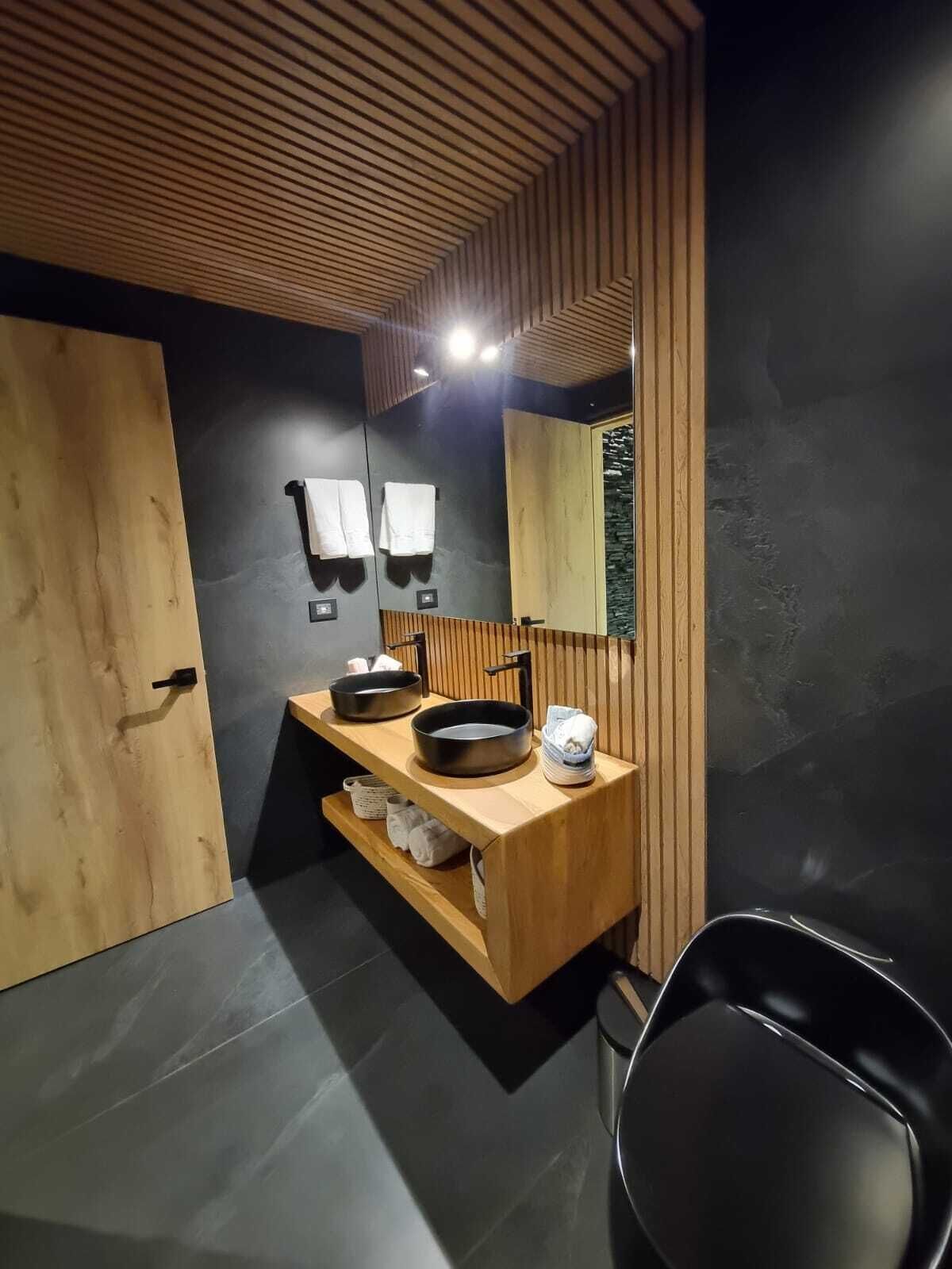 Een moderne badkamer met een houten wastafelmeubel, een zwarte wasbak en een spiegel.