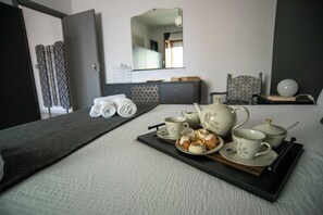 Un letto rifatto con cura, un vassoio con tè e pasticcini, un comò con uno specchio e una poltrona a fantasia.