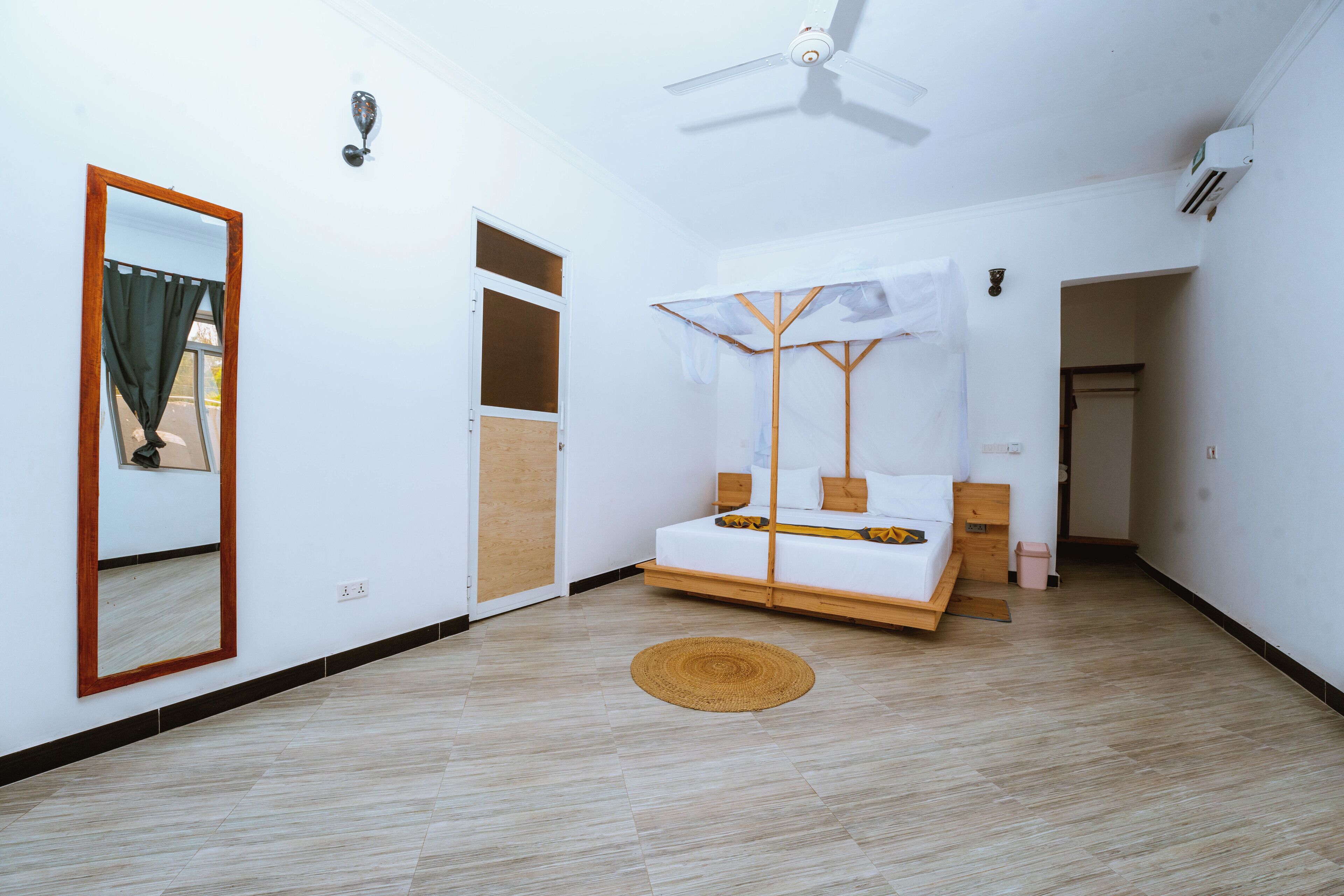 A bedroom with a bed, a ceiling fan, a mirror, and a door.