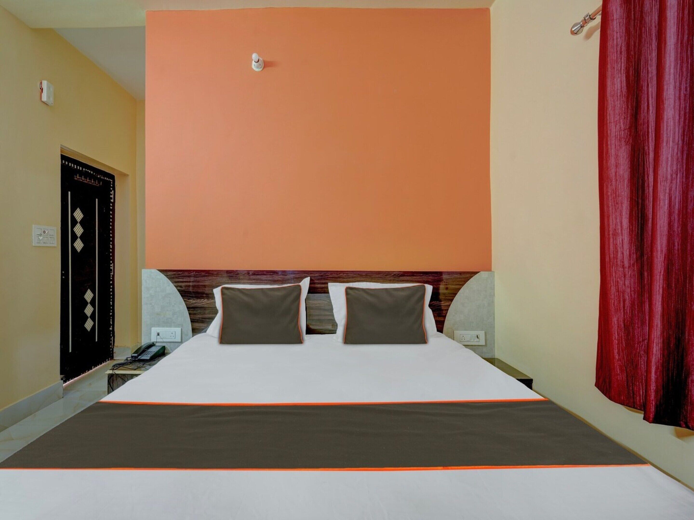 A hotel room with a large bed, two pillows, a wooden headboard, and a red curtain.