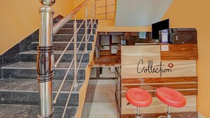 A staircase with a metal handrail and a wooden handrail, leading to a reception area with a wooden desk and two red stools. - Super Hotel O Siddhi Vinayak Hotel & Banquets (Motihari)