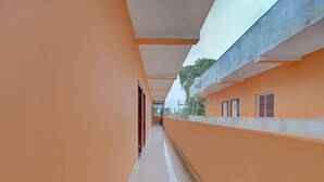 A corridor with orange walls and a tiled floor, leading to a building with a flat roof and a window with bars. - Super Hotel O Siddhi Vinayak Hotel & Banquets (Motihari)