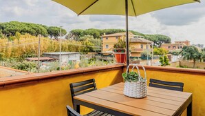 A balcony with a yellow umbrella, a wooden table, and two chairs.