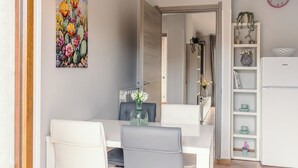 A dining area with a white table and chairs, a vase with flowers, and a painting of cacti on the wall.