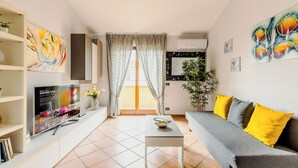 A modern living room with a flat-screen TV, a sofa with yellow cushions, a coffee table, and artwork on the walls.