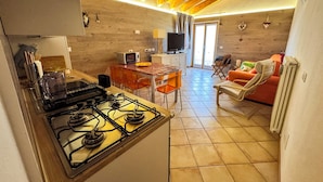 A compact kitchen with a gas stove, a dining area with a table and chairs, and a living area with a sofa and a television.