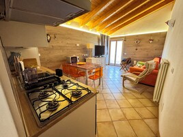 Una cocina compacta con estufa a gas, un comedor con mesa y sillas, y una sala de estar con sofá y televisor.