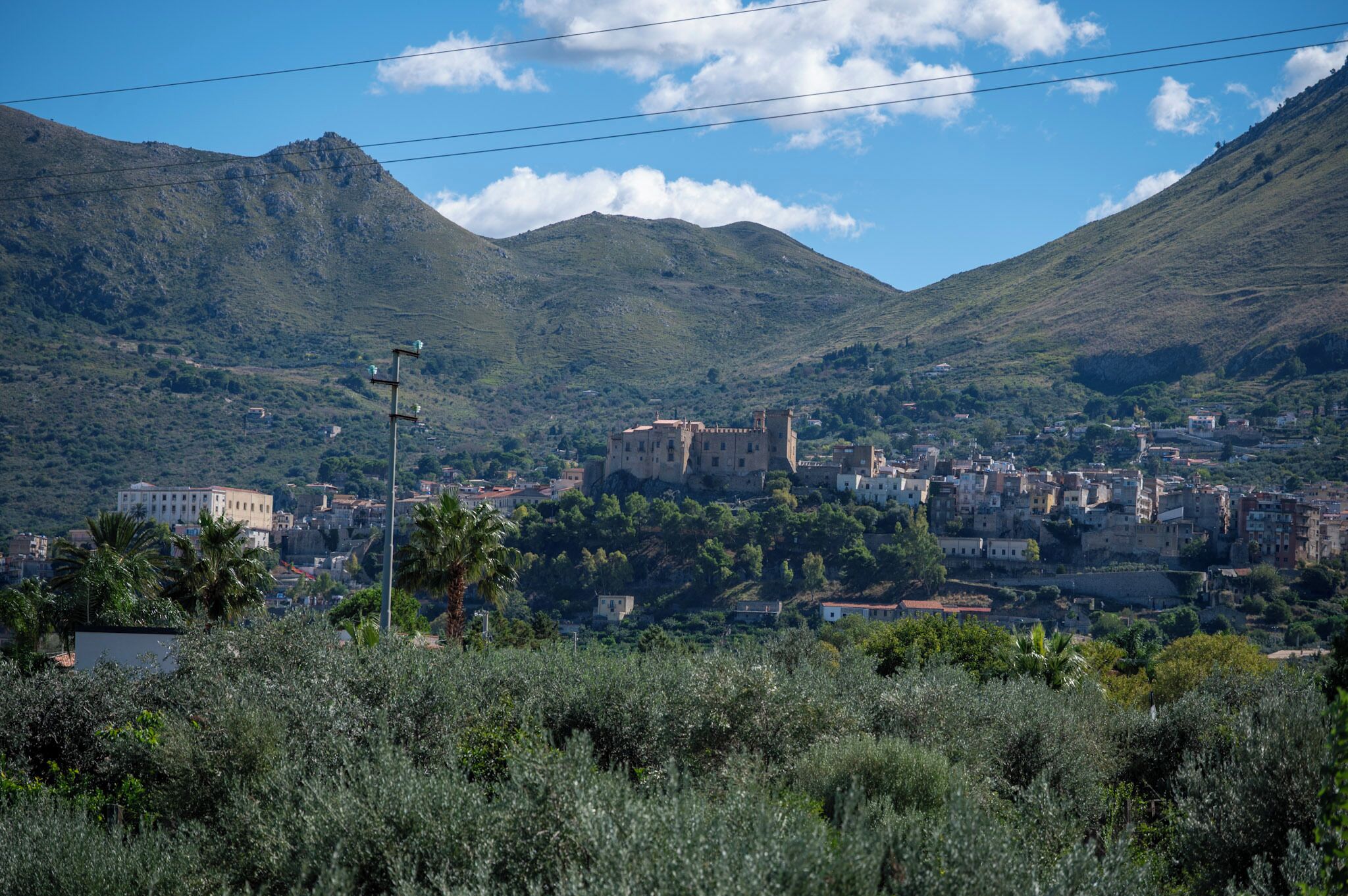 A town with a historic castle surrounded by mountains and dense greenery.