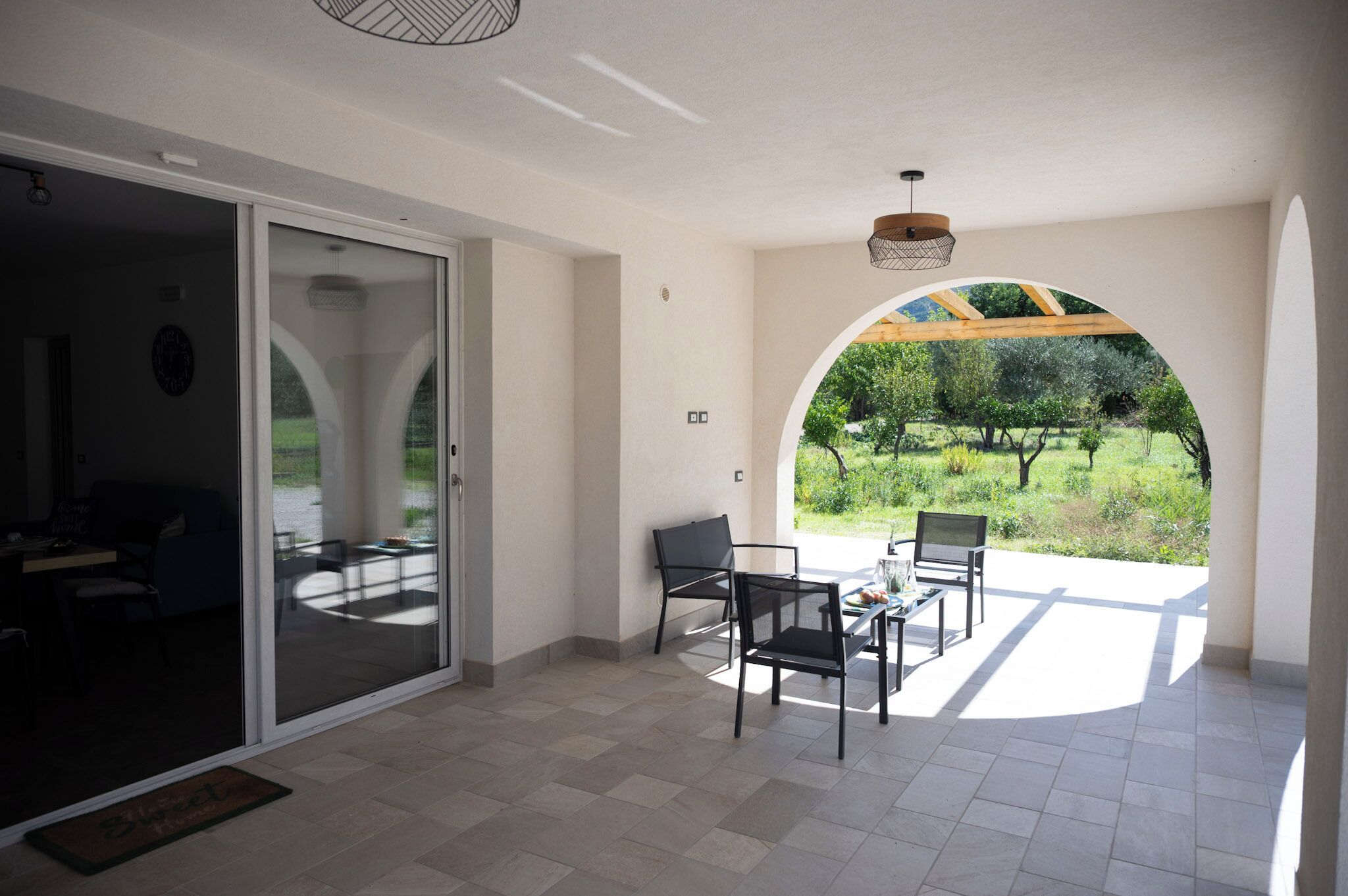 A spacious patio with a glass door leading to a garden, a table with chairs, and a view of greenery.