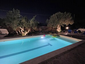 A swimming pool at night with a clear water surface, surrounded by trees and a few lounge chairs. - Villa Verde- Nature Holiday Home (Carini)