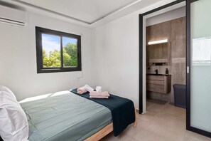 Ein Schlafzimmer mit Bett, einem Fenster mit Blick auf Grünflächen und einem Badezimmer mit Waschbecken und Spiegel.