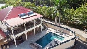 Un edificio de dos pisos con techo rojo, piscina y mobiliario exterior.