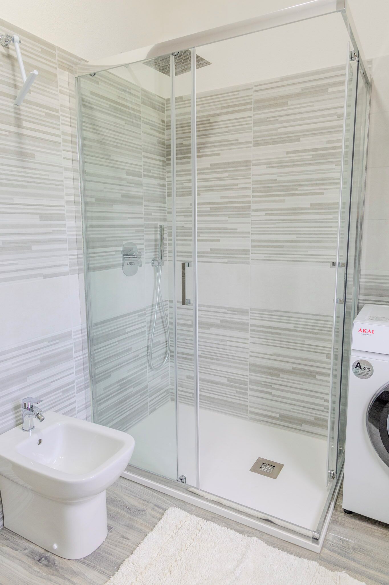 A modern bathroom with a glass-enclosed shower, a white bidet, and a washing machine.