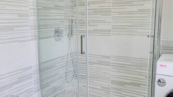 A modern bathroom with a glass-enclosed shower, a white bidet, and a washing machine.
