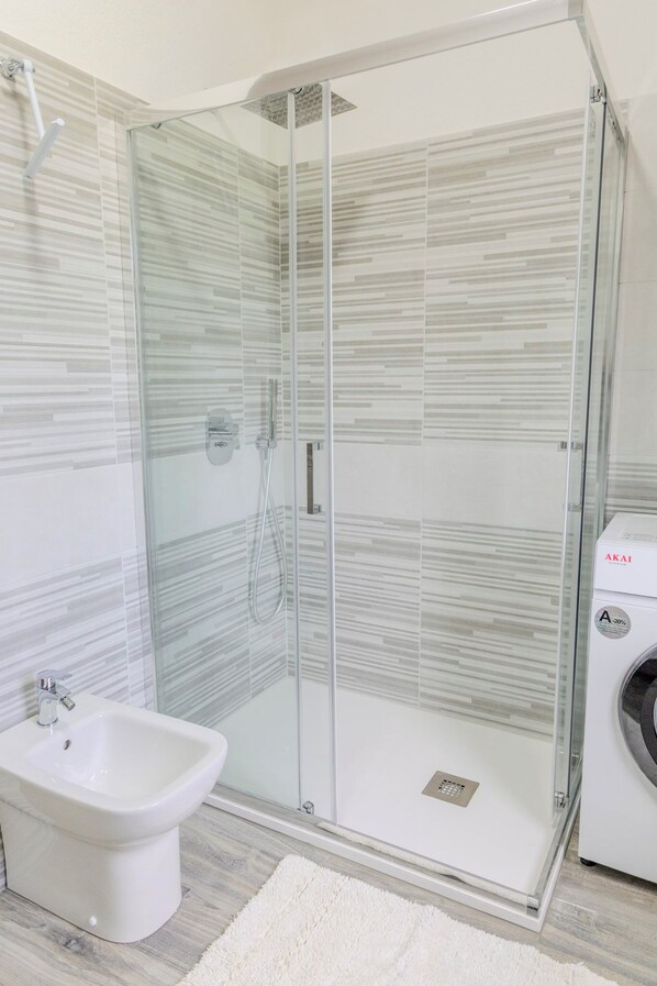 A modern bathroom with a glass-enclosed shower, a white bidet, and a washing machine. - Casa Vacanze Alessio (Nusco)