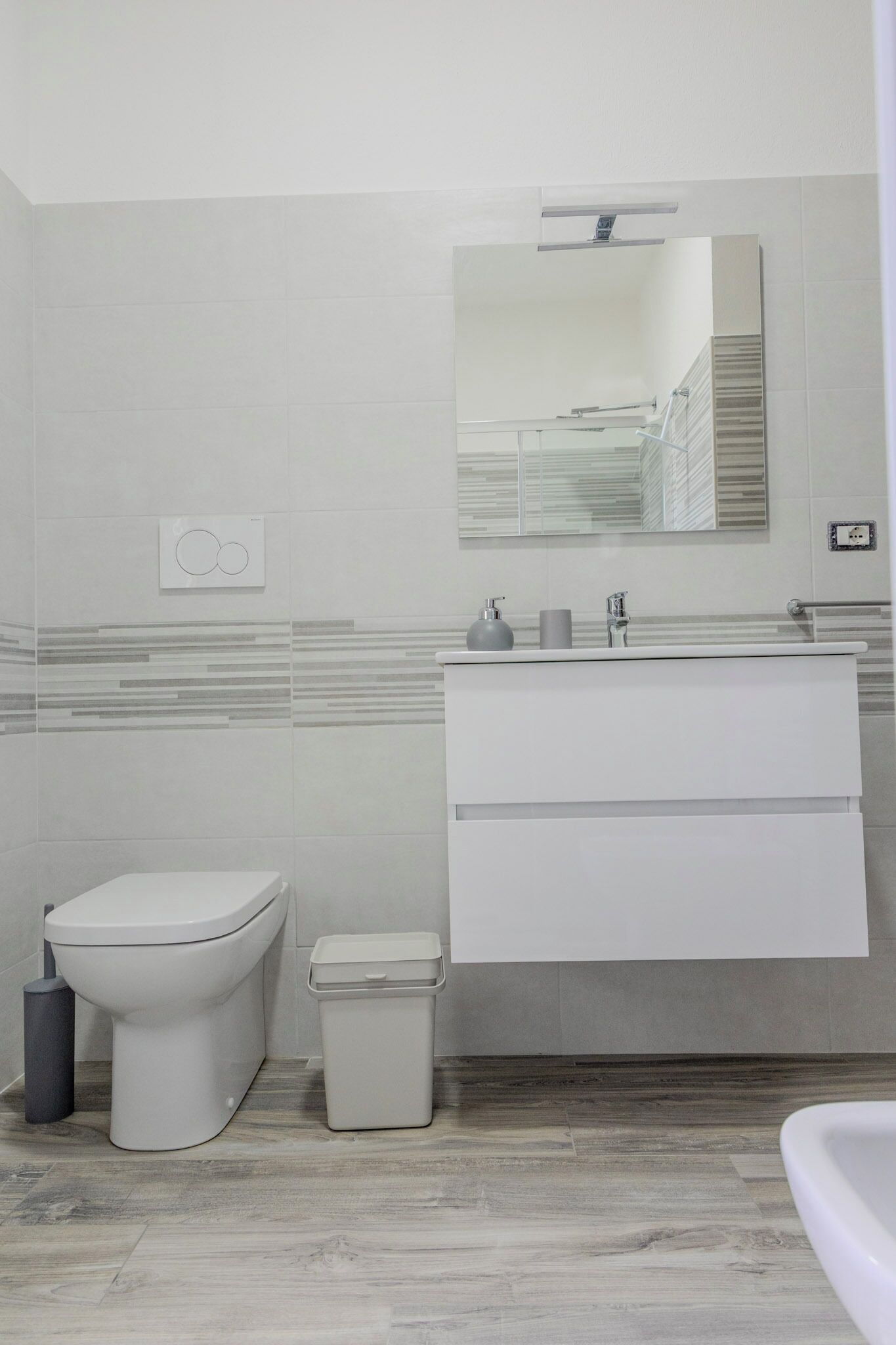 A modern bathroom with a toilet, bidet, sink, and mirror.