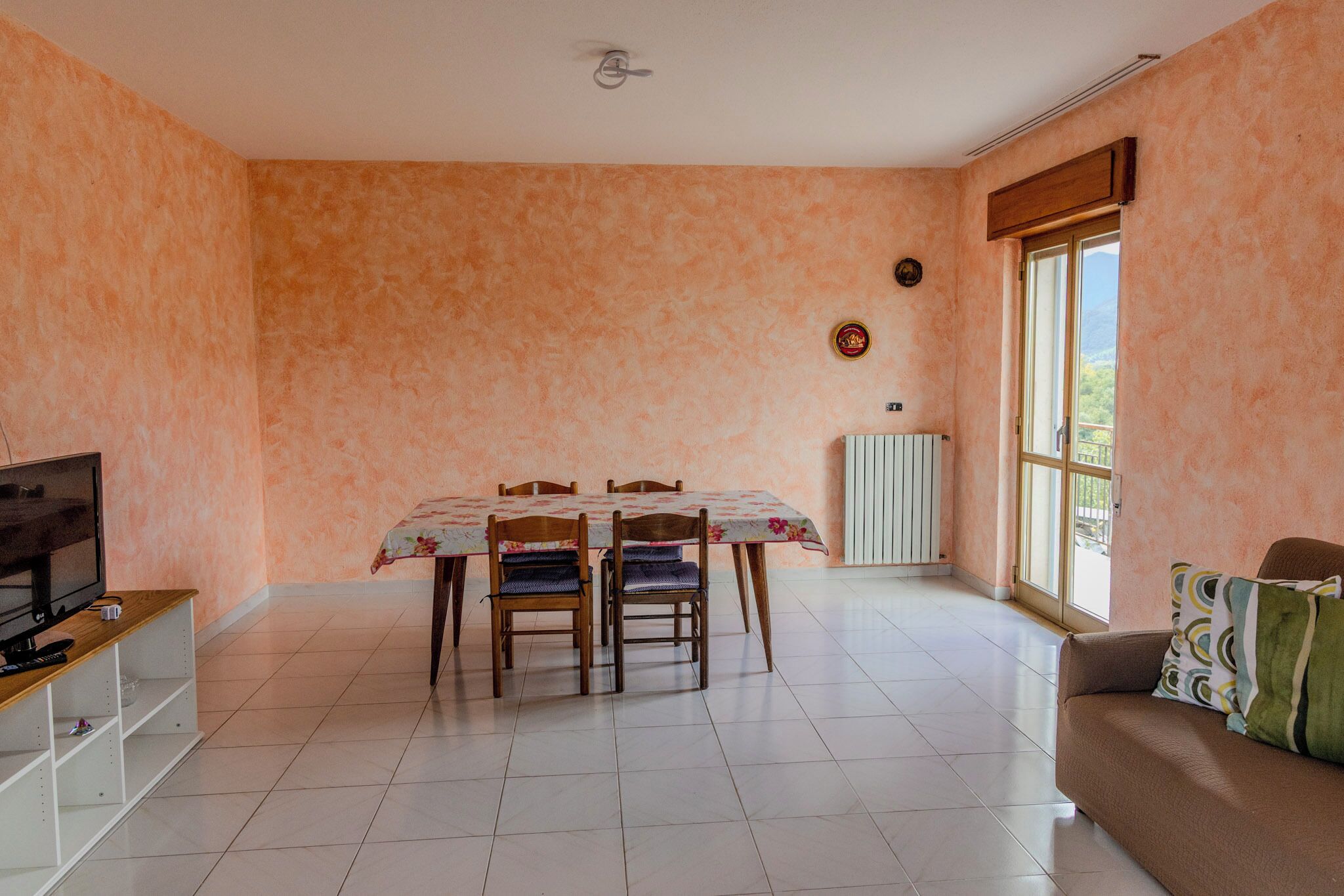 Un salon comprenant une table à manger, des chaises, un canapé, un téléviseur et une fenêtre donnant sur un beau paysage.
