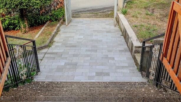 A paved pathway leading to a building entrance with a metal railing on one side and a wooden fence on the other. - Casa Vacanze Alessio (Nusco)