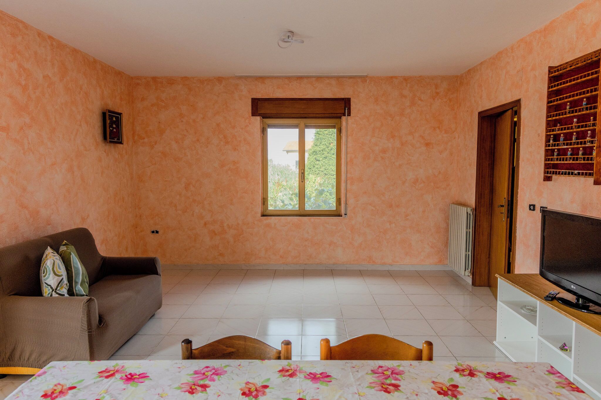 Een kamer met een bank, een tafel met stoelen, een televisie op een meubelstuk, een raam en een radiator.