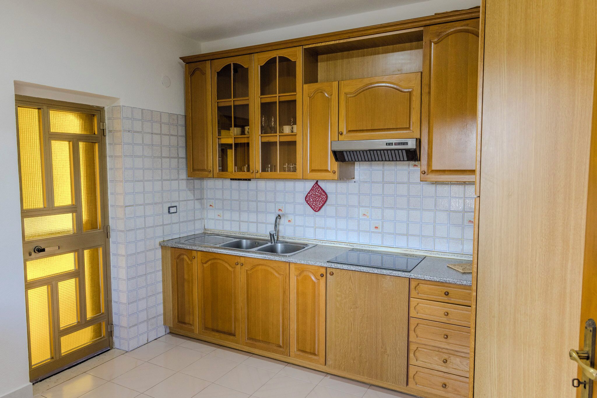 Een keuken met houten kastjes, een dubbele spoelbak en een betegelde spatwand.