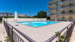 A swimming pool with a tiled deck, surrounded by a metal railing, and adjacent to a multi-story building with balconies. - Cariddi (Caulonia)