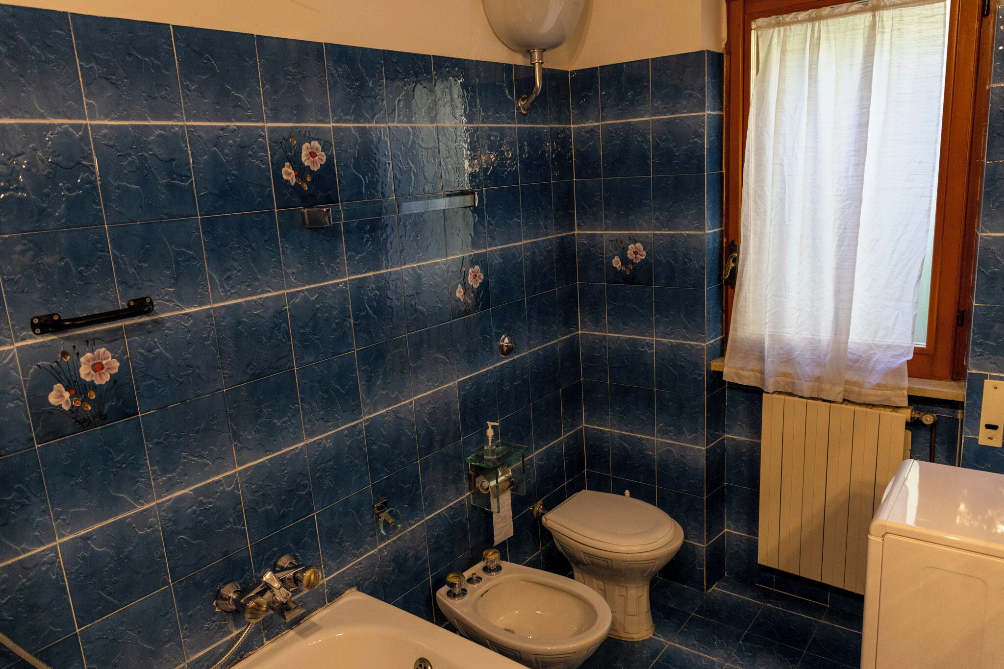 A bathroom with blue tiles, a toilet, a bidet, and a bathtub.