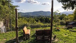 Un espacio de descanso al aire libre de estilo rústico con bancos de madera y una valla, rodeado de follaje y montañas al fondo.