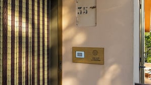 Una entrada de edificio con una reja metálica, una placa de número fijada en la pared y un pequeño ventanal.