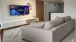 A modern living room with a large flat-screen TV mounted on the wall, a beige sofa, and a minimalist design. - Beautiful House in Maceió - 5 minutes from the Airport - 24-hour Check-in (Maceió)
