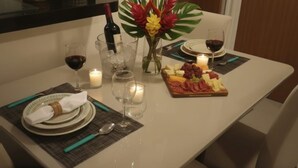 A dining table set with plates, cutlery, glasses, a bottle of wine, a candle, and a fruit platter. - Beautiful House in Maceió - 5 minutes from the Airport - 24-hour Check-in (Maceió)