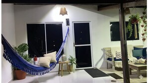 A cozy room with a hammock, a sofa, and a chair. There are two windows and a door. - Beautiful House in Maceió - 5 minutes from the Airport - 24-hour Check-in (Maceió)