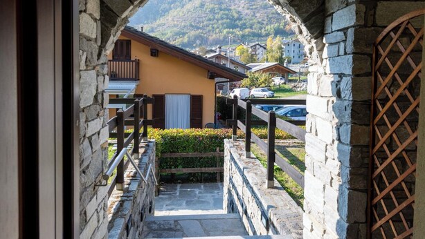 A stone archway leading to a building with a balcony, a wooden fence, and a view of a mountain. - La Maison De L'Adret (Saint-Pierre)