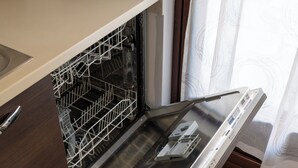 An open dishwasher with a metal rack inside, a control panel on the right, and a kitchen counter to the left. - La Maison De L'Adret (Saint-Pierre)
