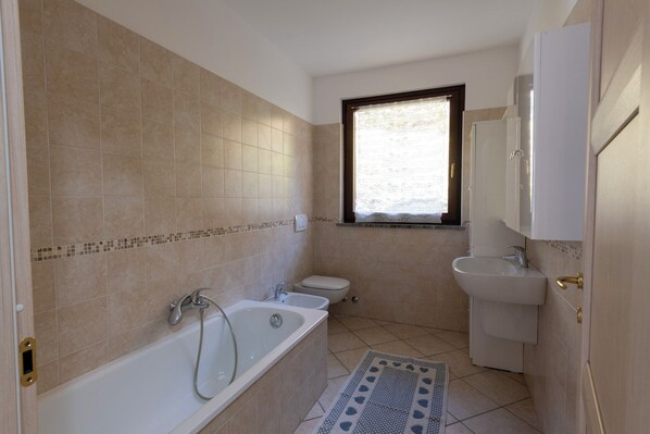 Une salle de bain avec une baignoire, des toilettes, un lavabo et une fenêtre.