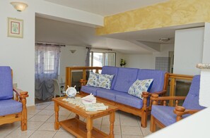 A living room with a sofa, two armchairs, a wooden coffee table, and a dining area visible in the background. - Mermaid - Cala Gonone (Cala Gonone)