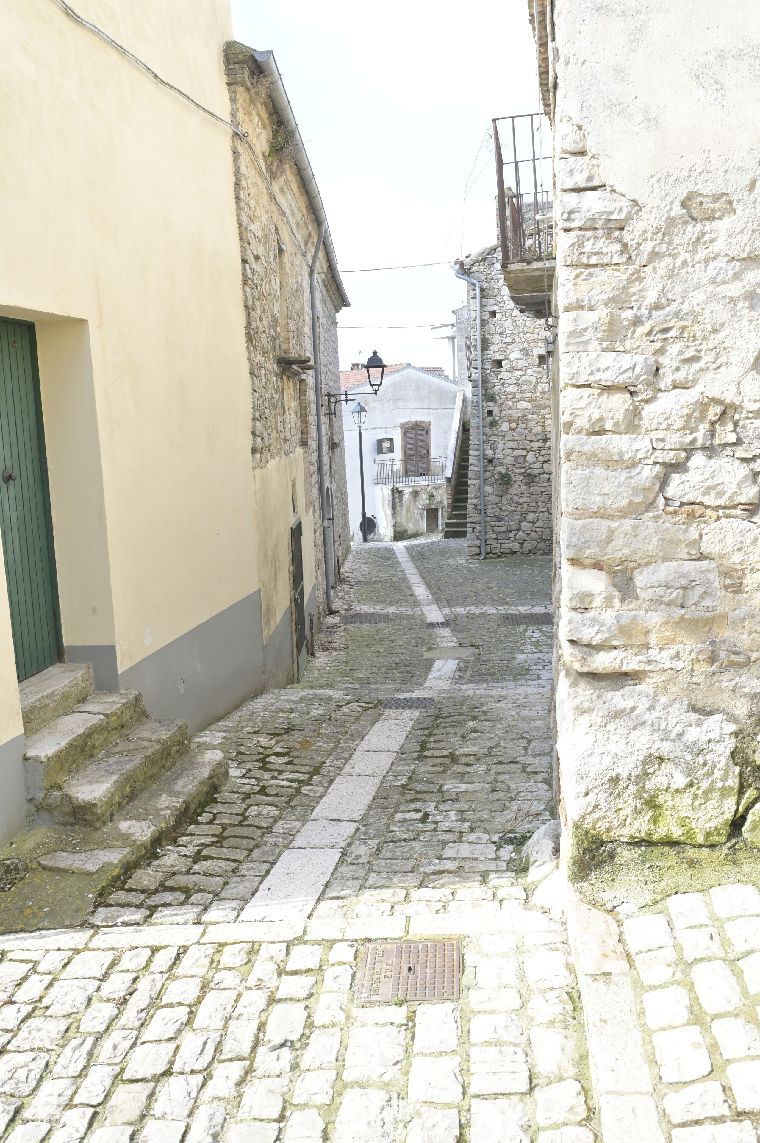 A narrow cobblestone street flanked by historic buildings with stone walls and a green door.