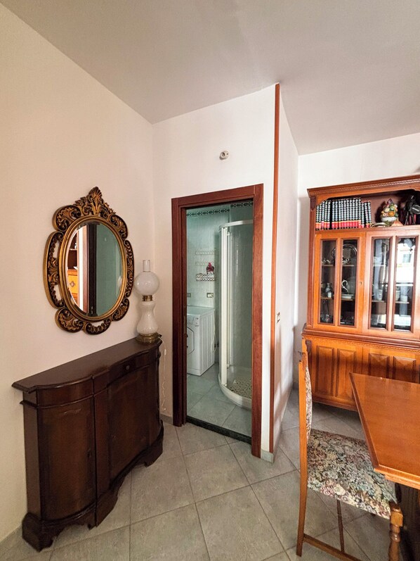 Una habitación con un armario de madera, un espejo, una mesa de comedor con mantel individual estampado y un aparador con libros.