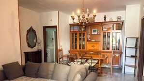 Una sala de estar con sofá, mesa de comedor, sillas, una araña y un aparador de madera con puertas de cristal.